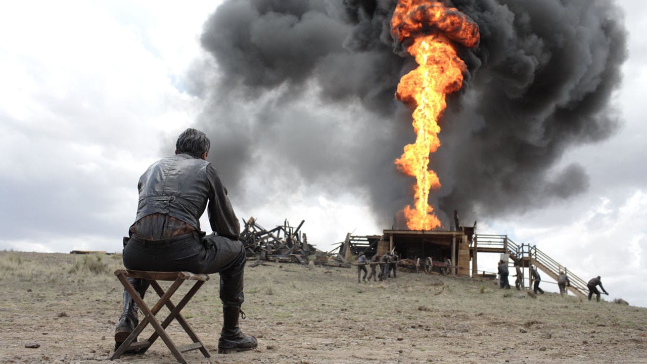 Daniel Plainview (Daniel Day-Lewis) assis devant un puit de pétrole en feu dans There Will Be Blood