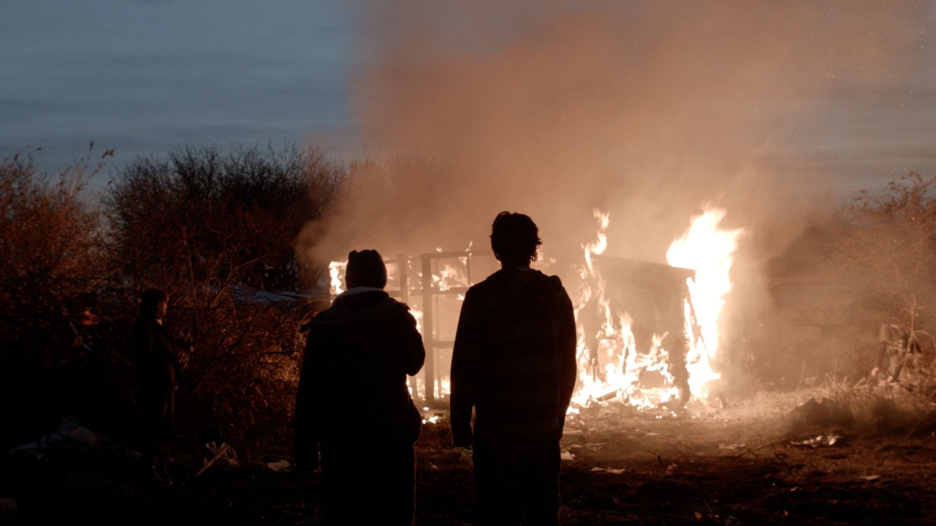 Des migrants regardent leur maison bruler dans la jungle de Calais dans L’Héroïque lande, la frontière brûle