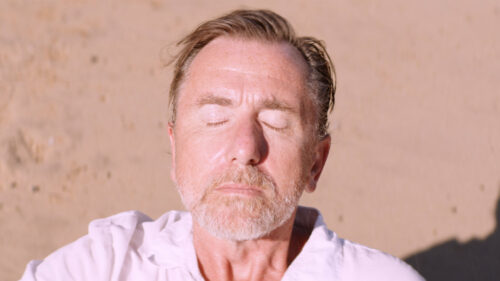 Neil Bennett (Tim Roth) prend le soleil sur la plage dans Sundown