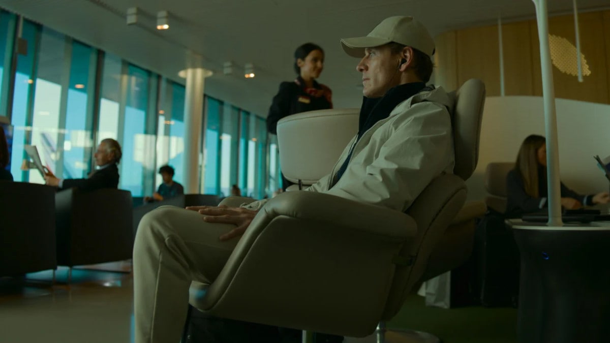 Le tueur (Michael Fassbender) assis dans un divan avec son imperméable dans The Killer