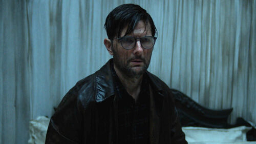 Ohm Bauman (Adam Scott) au milieu du lit dans la suite dans Hokum